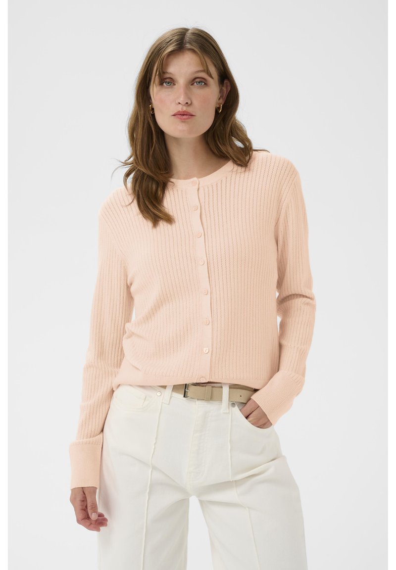 Hellrosa gerippte Strickjacke mit Knopfleiste, langen Ärmeln und rundem Ausschnitt, kombiniert mit weißen, hoch taillierten Hosen.