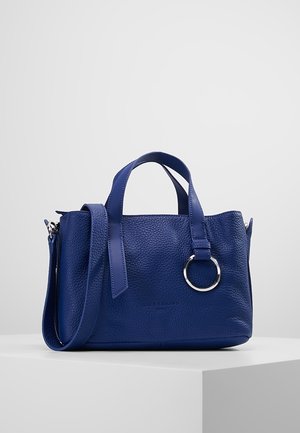 Niebieska torebka ze skóry z fakturą, z podwójnymi uchwytami, odpinanym paskiem na ramię i srebrnym pierścieniem na froncie, umieszczona na białym piedestale.