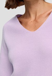 Pull en tricot lavande avec un col en V, présentant une texture côtelée et une finition douce, mettant en valeur une coupe confortable et décontractée.