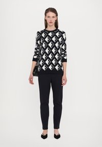 Svart-hvitt geometrisk mønstrete genser med lange ermer, kombinert med svarte slim-fit bukser og svarte spisse flats.