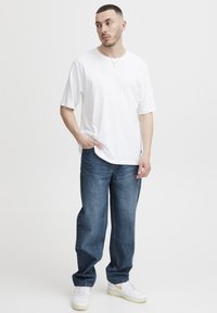 Balta kokvilnas T-krekls ar īsām piedurknēm, kopā ar zilām džinsa biksēm un baltiem sporta apaviem ar dzelteniem akcentiem. Vienkāršs dizains, brīvs piegriezums.