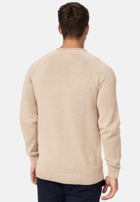 Suéter de punto beige con dobladillo y puños acanalados, con escote de cuello redondo y mangas ranglán, que muestra un tejido texturizado.