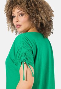 Groene T-shirt met een relaxte pasvorm, geplooide korte mouwen met trekkoordsluiting en een zachte, gladde textuur.