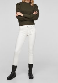 Oliwkowy pulower z bufkami, zestawiony z białymi, dopasowanymi dżinsami i czarnymi botkami za kostkę, z zamkiem i płaską podeszwą.
