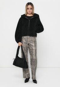 Must värviline kunstkarusnaha jakk, mustrilised maosülesed püksid ja must käekott. Mudel kannab elegantselt musti kontsakingi ja läbipaistvaid prille.