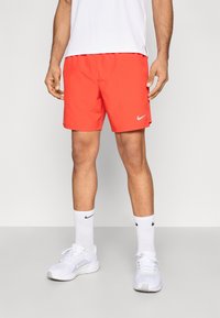 Κόκκινα σορτς Nike με ελαστική μέση, πλαϊνές τσέπες και μικρό ασημί λογότυπο. Συνδυασμένα με λευκά αθλητικά παπούτσια και κάλτσες. Απλός σχεδιασμός.