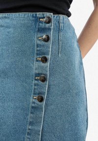 Denimrok met een hoge taille, lichtblauwe kleur en een rij van zes zilveren knopen aan de zijkant, met zichtbare stiksels en een gestructureerde afwerking.