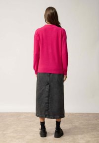 Fuchsiastrickpullover mit langen Ärmeln, kombiniert mit einem schwarzen Denim-Midikleid mit einer Mittelnaht und knöchelhohen schwarzen Schuhen.