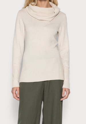 Beige Strickpullover mit Kaskadenkragen, langen Ärmeln, gerippten Bündchen und einem etwas längeren hinteren Saum, kombiniert mit loser grüner Hose.