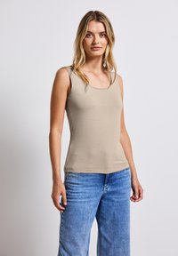 Top senza maniche color beige con scollo tondo e design aderente, abbinato a jeans a gamba larga blu chiaro. Texture liscia, stile casual.