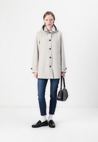 Lys grå regnjakke med hette, svarte knapper og to frontlommer. Brukt over blå jeans og svarte loafers, med en liten svart veske.