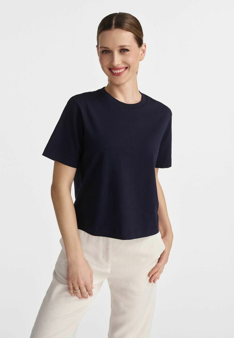 Granatowa bawełniana koszulka z krótkim rękawem i okrągłym dekoltem o luźnym kroju, zestawiona z jasnymi lnianymi spodniami.