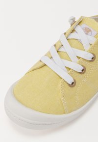 Bottines en toile jaune avec lacets blancs, bout rond et tige texturée. Présente des œillets en métal et une semelle en caoutchouc avec des détails de couture.