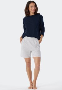 Marineblauw shirt met lange mouwen, gecombineerd met lichtgrijze shorts met een elastische tailleband. De stof lijkt zacht en heeft een casual pasvorm. Persoon staat blootvoets.