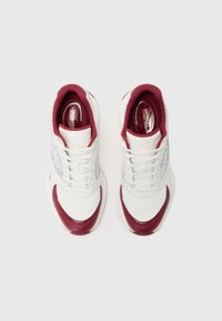 Bílé tenisky s červenými akcenty, texturovanou síťovinou a hladkou kůží. Obsahují šněrovací design a detail loga na boku.