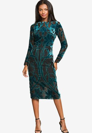 Zwart langemouwen jurk met teal bloemenpatroon, doorschijnende overlay, slank ontwerp, knielang en gecombineerd met zwarte hoge hakken.
