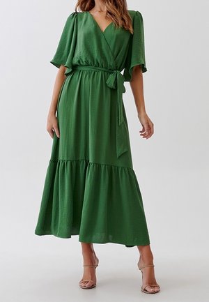 Zielona sukienka o kroju kopertowym z krótkimi falbaniastego rękawami, dekoltem w szpic, wiązaniem w talii oraz warstwowym dołem. Wykonana z lekkiego materiału o miękkiej fakturze.