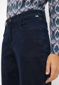 Mørkeblå jeans med en glat tekstur, der har et klassisk fem-lomme design og en metalknap lukning i taljen.
