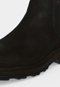 Gros plan d’une botte en cuir noir montrant la tige lisse, le détail des coutures et la semelle en caoutchouc texturée.