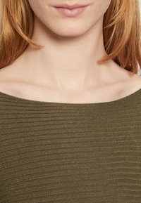 Olive green ribbed top with a wide neckline. The texture is soft and slightly stretchy, revealing collarbone and smooth skin beneath.