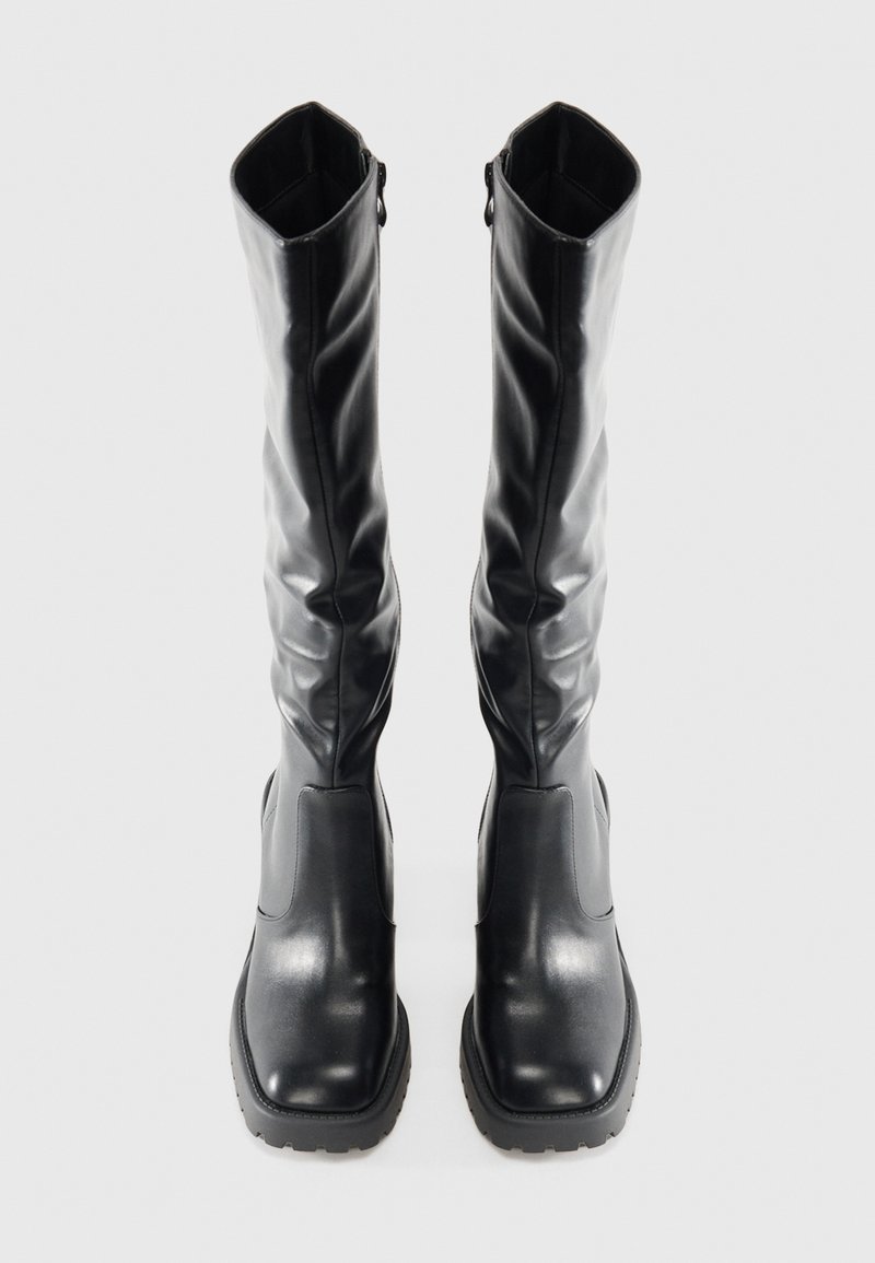 Bottes noires jusqu'au genou en cuir lisse avec une semelle épaisse, présentant un design ajusté et une fermeture éclair discrète sur le côté.