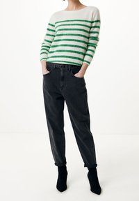 Randig tröja i vitt och grönt, kombinerad med mörkgrå tapered jeans. Svarta ankelstövlar fulländar looken. Mysig textur, avslappnad design.