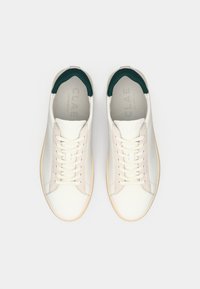 White sneakers with a smooth leather upper, contrasting green heel accents, and a beige rubber sole. Features a lace-up design.