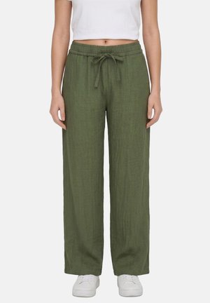 Donna che indossa pantaloni di lino verde oliva a gamba larga con vita con coulisse, abbinati a sneakers bianche e top bianco corto.