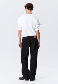 Sorte, løstsiddende bukser med højt liv, der har to baglommer og en læderlap på bageste linning. Kombineret med en hvid rundhalset skjorte.