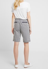 Pruhované bermudské šortky v šedé a bílé barvě, s uvolněným střihem, zadními kapsami a hladkým povrchem; stylizované s jednoduchým bílým topem.