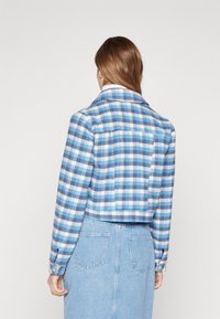 Kratka modra karirana jakna z mehkimi vlakni, gumbi na zapestjih in klasičnim ovratnikom. Obučena čez svetlo denim krilo.