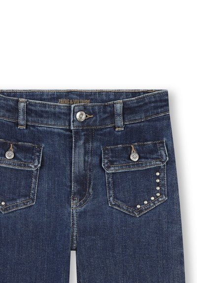 Jean en denim bleu foncé avec une taille mi-haute, présentant des accessoires en métal argenté, deux poches arrière et des clous décoratifs semblables à des perles sur une poche.