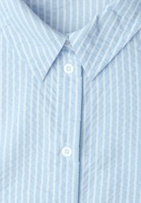 Col de chemise bleu clair avec des rayures blanches verticales et deux boutons blancs sur une patte boutonnée.