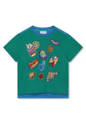 Camisa verde de manga corta con ribete azul, decorada con parches coloridos que incluyen una lata de refresco, dados, perrito caliente, coche y símbolos gráficos.