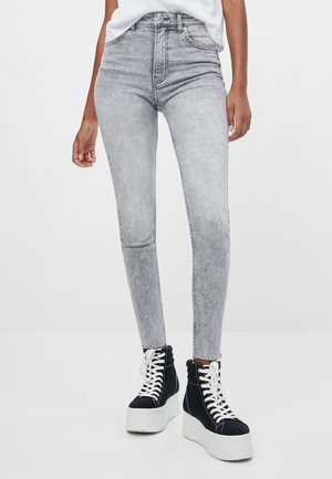 Person iført lysegrå high-waisted skinny jeans kombineret med sorte platform snøresko og en indstukket hvid top.