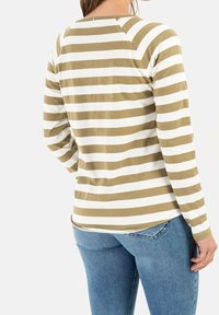 Personne portant une chemise à manches longues rayée beige et blanche à l'horizontale et un jean bleu, vue de dos sur un fond uni.