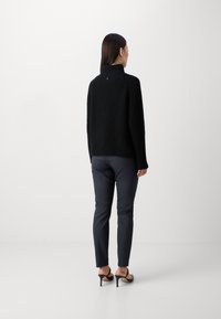 Pulover negru din tricot cu nervuri, cu guler înalt, asortat cu pantaloni navy ajustați și sandale negre cu toc. Design minimalist și linii curate.