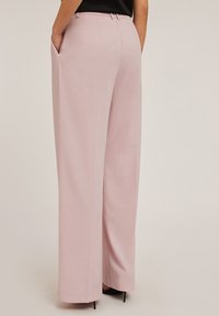 Lichtroze wijde broek met een soepele textuur, zijzakken en een getailleerde pasvorm. De tailleband heeft riemlussen.