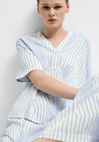 Set di pigiama a righe azzurro e bianco in morbido tessuto. Presenta una maglietta con scollo a V e maniche corte, oltre a una tasca. Vestibilità ampia.