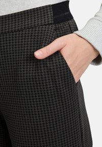 Schwarz-graue karierte Hose aus einem weichen, texturierten Stoff, mit einer Seitentasche und einem elastischen Bund für zusätzlichen Komfort.