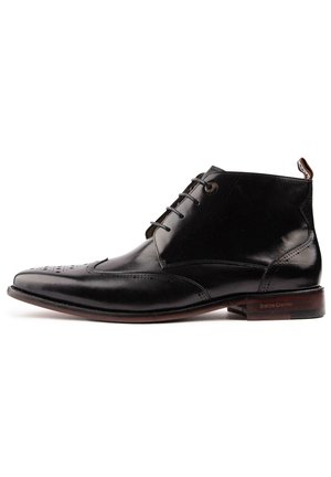 Black leather men's dress boot with brogue detailing, laces, and a brown sole, shown in side profile on a white background.