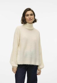 Krämfärgad polo-tröja med lös passform, ribbad textur och vida �ärmar, kombinerad med mörka denimjeans. Mjuk, varm material.