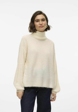 Cremfarbener Rollkragenpullover mit lockerer Passform, geripptem Muster und weiten Ärmeln, kombiniert mit dunklen Jeans. Weiches, kuscheliges Material.