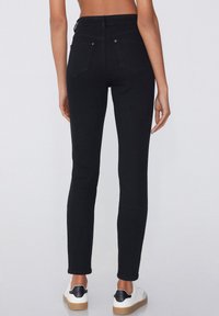 Jeans skinny en denim noir taille haute, dotés de deux poches arrière et de détails de couture minimalistes. Associés à des baskets blanches.