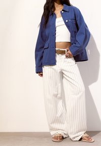 Blue cotton jacket over a white crop top, paired with white pinstriped wide-leg pants and tan flip-flops, featuring a simple belt.