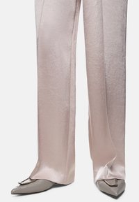 Pale pink satin wide-leg trousers paired with pointed gray heels featuring a metal accent. Smooth texture with subtle sheen.