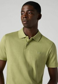 Ljusgrön polo-shirt i texturerat tyg, med treknappslåstning, korta ärmar och liten logotyp på bröstet.