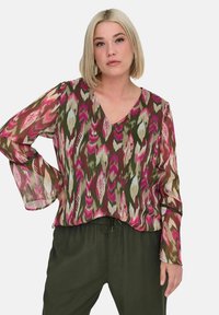 Blusa multicolore con scollo a V, maniche lunghe fluide e motivo astratto ikat in tonalità di rosa, verde e beige. Tessuto leggero e trasparente.