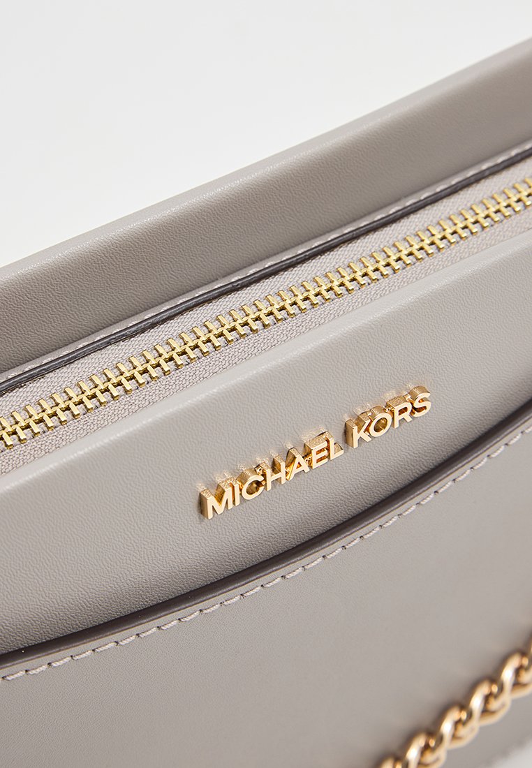 Grijze leren handtas met gouden hardware, voorzien van een ritsluiting en het gegraveerde logo "MICHAEL KORS" aan de voorkant.