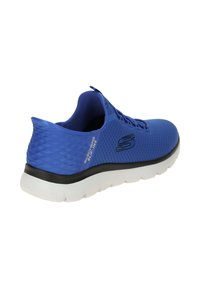 Chaussure de sport Skechers bleu à enfiler avec dessus en mesh, logo noir sur le côté et semelle blanche texturée, vue en angle montrant le talon et le côté.